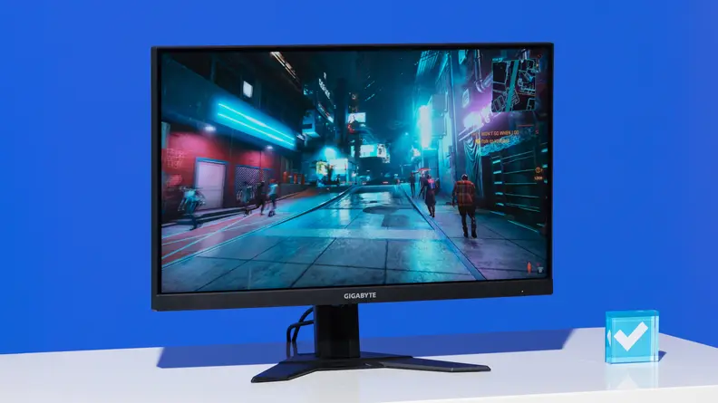 A large computer monitor standing upright on a white desk aganist a blue background.