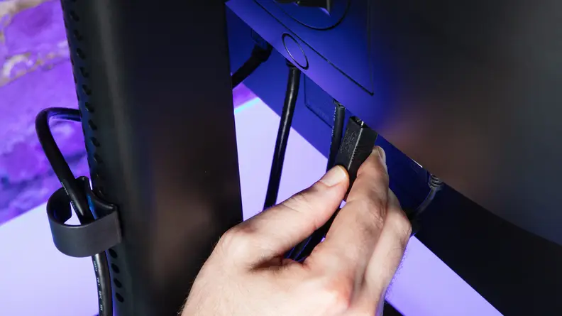 A hand plugs a USB cable into a USB port in the back of the NZXT Canvas 27Q.