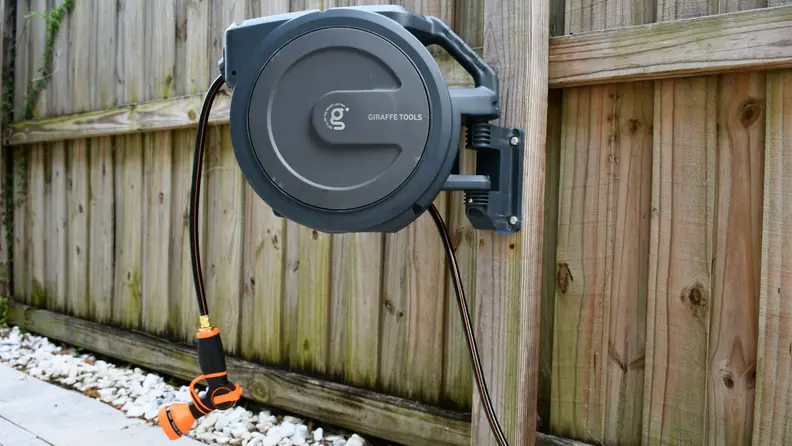 The Giraffe Tools Retractable Garden Hose Reel hangs on a fence in a backyard