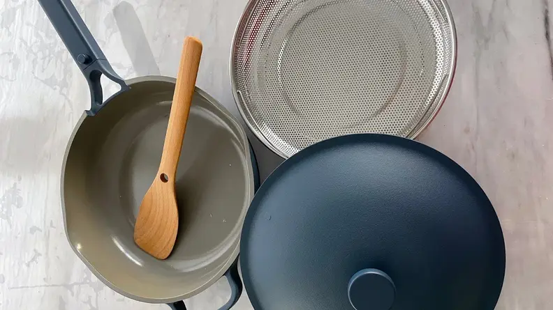 Always Pan 2.0 in Blue Salt color with lid, wooden spoon and steaming basket next to it.