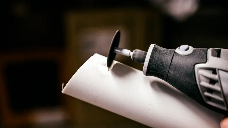 Person uses a dremel 8220 on white pipe