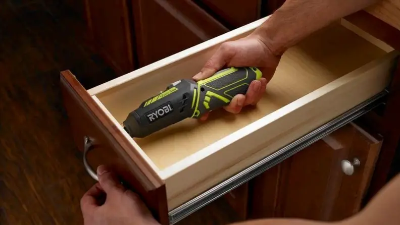 a person uses an electric screwdriver to attach the handle to a cabinet drawer