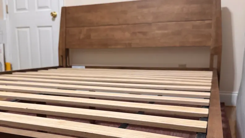 Brown wooden FlexiSpot Kana headboard and platform frame without a mattress, showing slats.