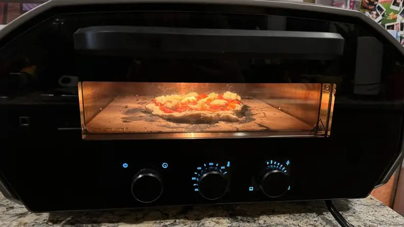 Raw pizza cooking inside of the Ooni Volt 12 pizza oven with door closed.