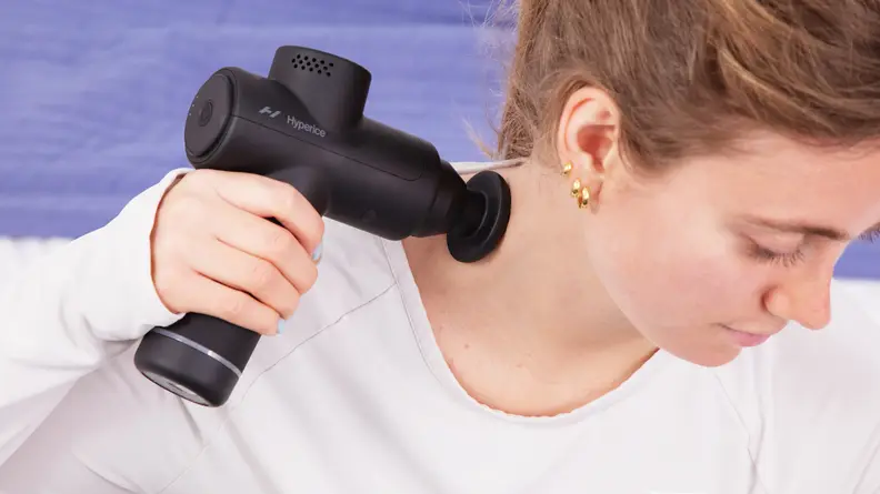 A woman putting the Hyperice Hypervolt 2 Go on her neck to massage it.