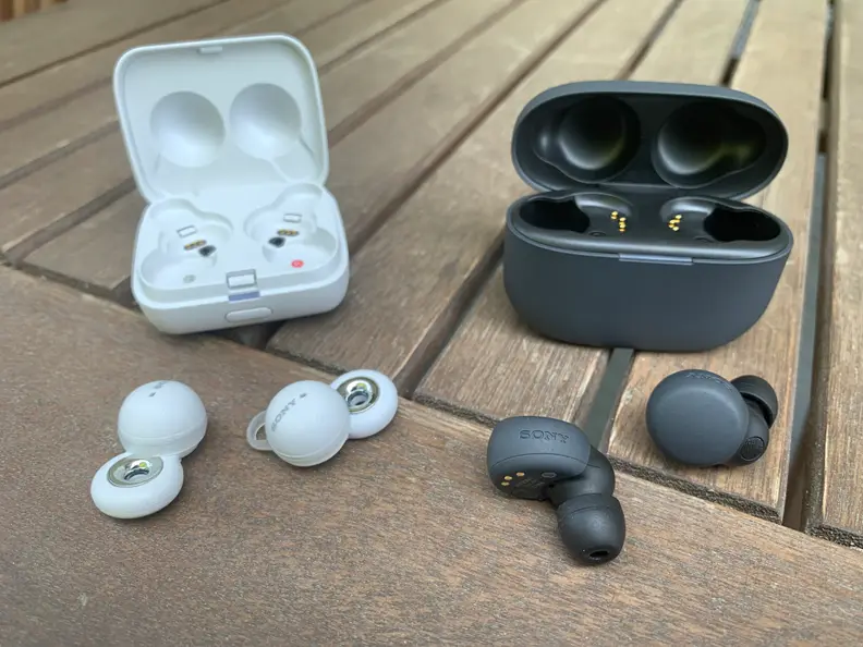 The black Sony LinkBuds S with their black charging case and the white Sony LinkBuds with their charging case sit on a wooden table.