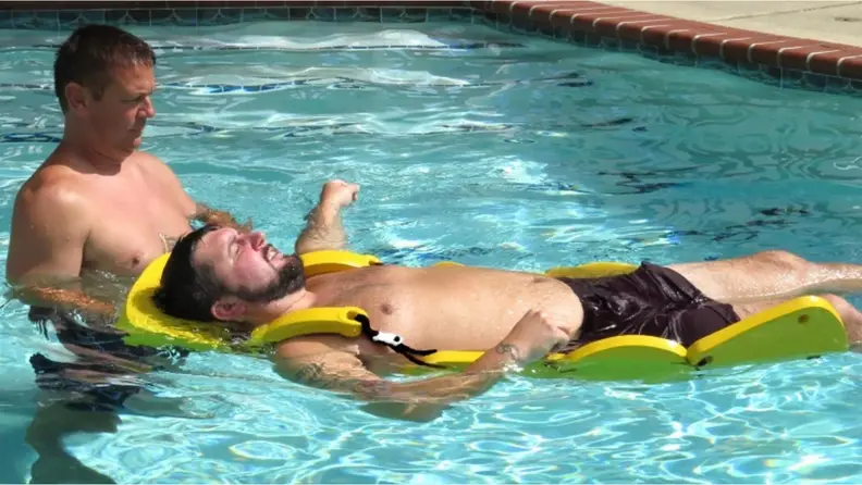 A man wearing the Danmar Sectional Raft Swim Aid while another man helps him around a pool.