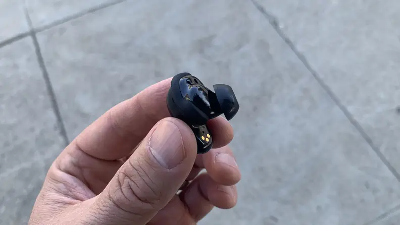 Close-up shot of a hand holding a Bose QuietComfort II earbud.