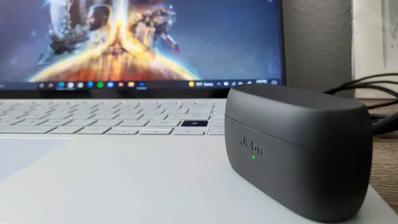 Jabra's all-black, matte earbuds sit in their open case on the silver surface of a laptop, with a space image glowing vividly in the background.