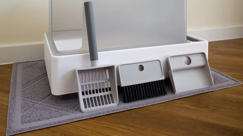 A scooper, brush, and handle lined up against the Cove litter box.