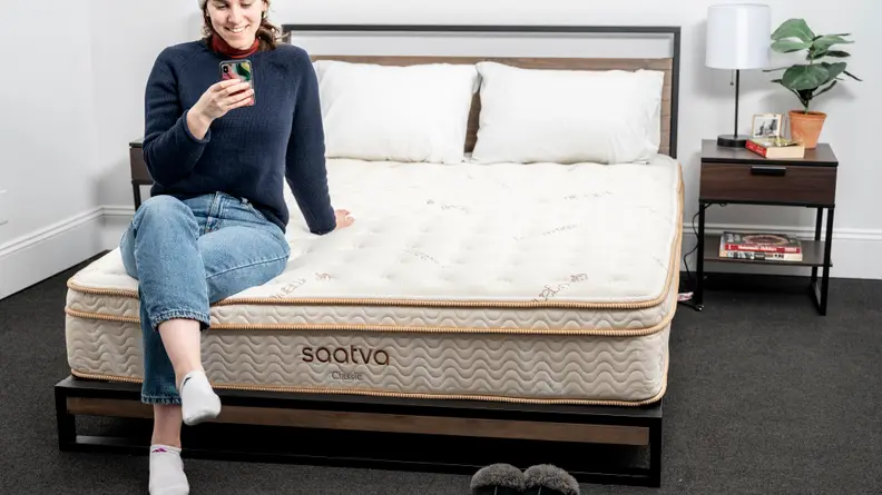 A person sitting on the bottom edge of the Saatva Classic mattress.