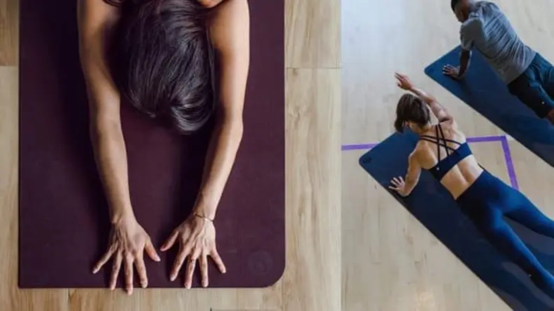 Left: Overhead view of a woman with arms stretched on a yoga mat. Right: A woman and man in athletic outfits stretching on a yoga mat.