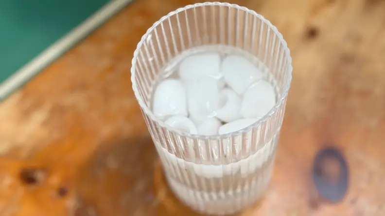 Glass of bullet-shaped ice water in a clear glass on a wooden surface.