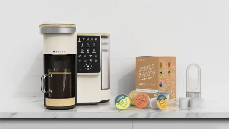 Bruvi coffee machine with mug full of coffee under dispenser next to box of coffee pods on marble countertop.