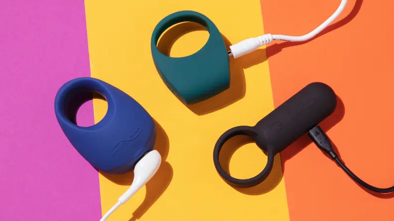 The We-Vibe Pivot, Lelo Tor 2 and Tenga SVR all hooked up to charging cords on top of a pink, yellow and orange surface.