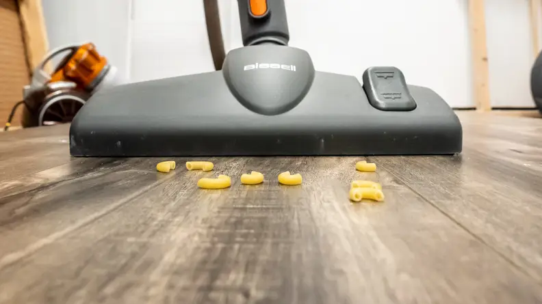 A vacuum tries to suck up macaroni spilled on hardwood floors