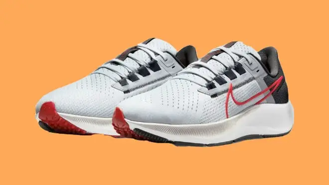 White, black and red Nike Air Zoom shoes in front of orange background.