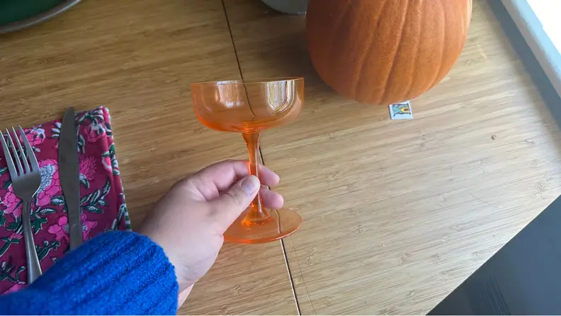 A hand holding an orange coupe on a dining room table.
