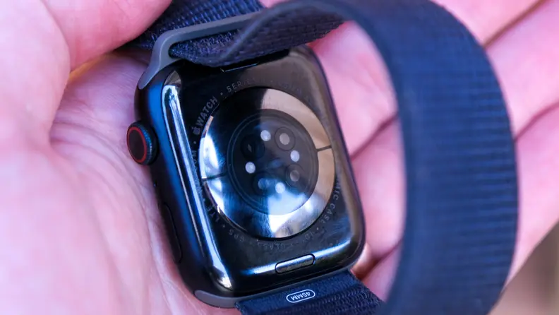 A reviewer holds an Apple Watch Series 9, showing off the health tracking sensors on the back of the watch.
