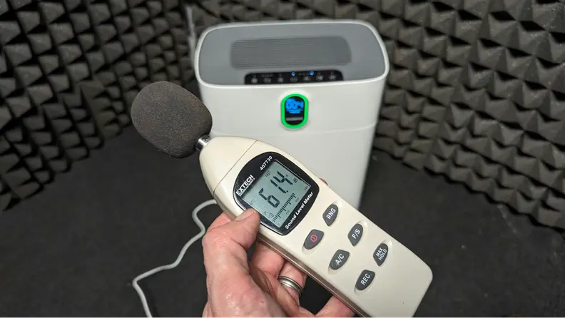A hand holds a sound level meter.