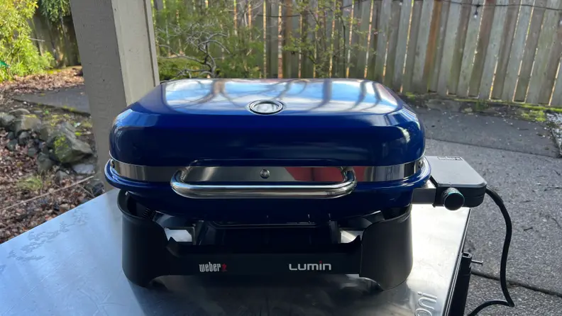 The Weber Lumin in Deep Ocean Blue sits on a table outdoors.