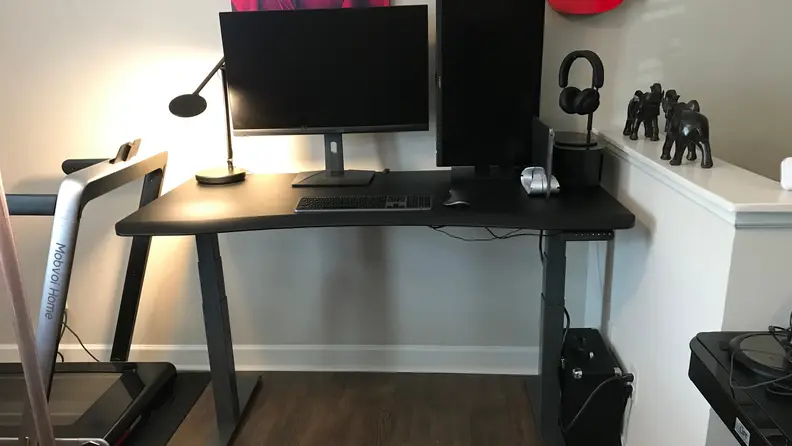 A computer desk with two monitors, a speaker, and keyboard in a living room.