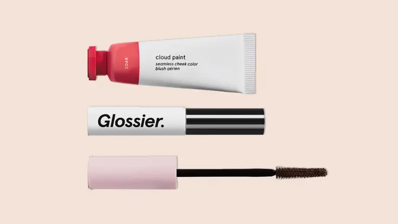 The Glossier "The Makeup Set" that includes Boy Brow, Cloud Paint and Lash Slick on a tan background.