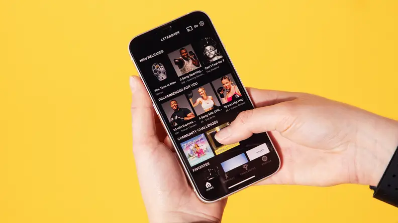 Person holding up smartphone featuring assorted fitness classes within the Liteboxer app.