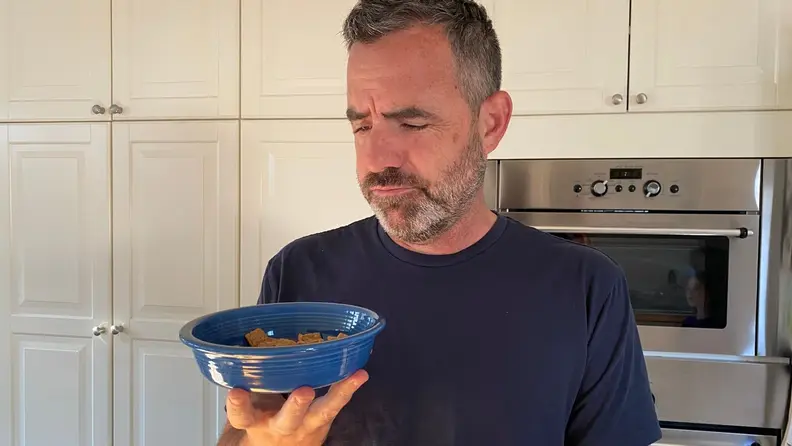 A man looks at a bowl of cereal, but it looks like dog food.