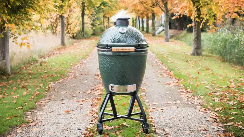 A Big Green Egg sits in the middle of a road surrounded by autumnal foliage.