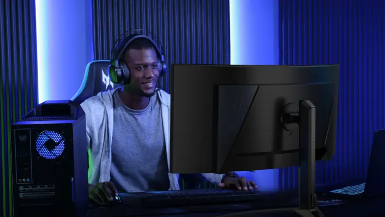 A person wearing headphones facing the camera smiles as they stare at an Acer ultrawide gaming monitors.