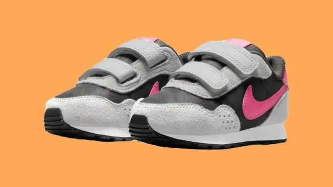 Black, white and pink Nike MD Valiant sneakers in front of orange background.