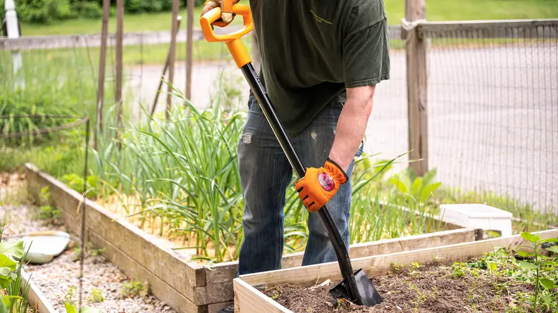 A person using a shovel in a garden bed