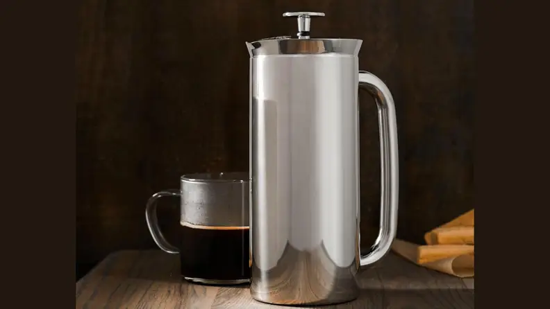 Espro French press besides a cup of coffee on a wooden surface