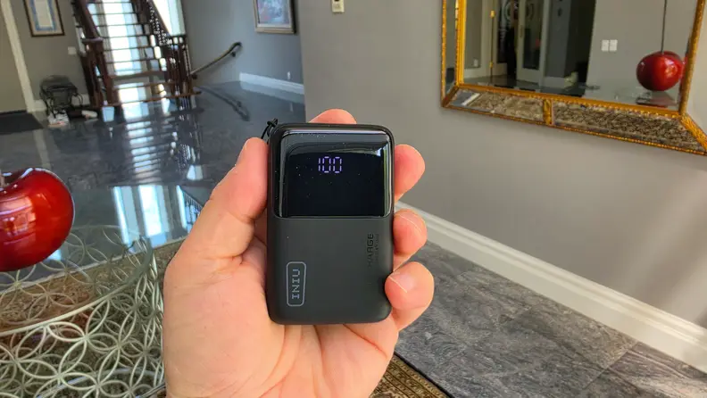 Black INIU Pocket Rocket 50 portable charger being held in a man's left hand in front of a grey wall with a mirror.