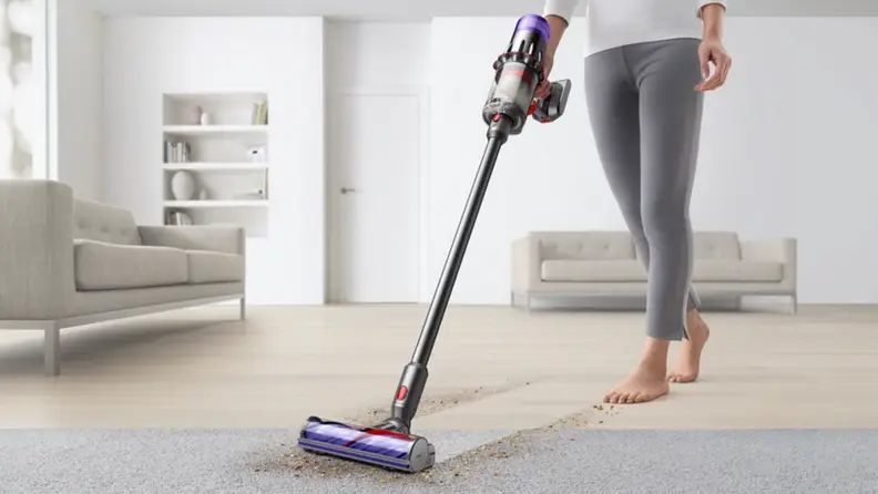 A person vacuums a carpet using a stick vacuum