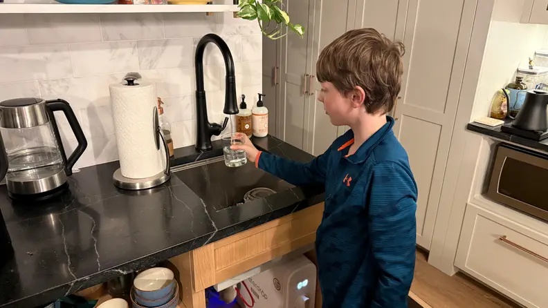 Child filling a glass of water at a kitchen sink connected to a Waterdrop G3P800 filtration system. Caption: The Waterdrop G3P800 provides clean, filtered water straight from your tap for everyday use.