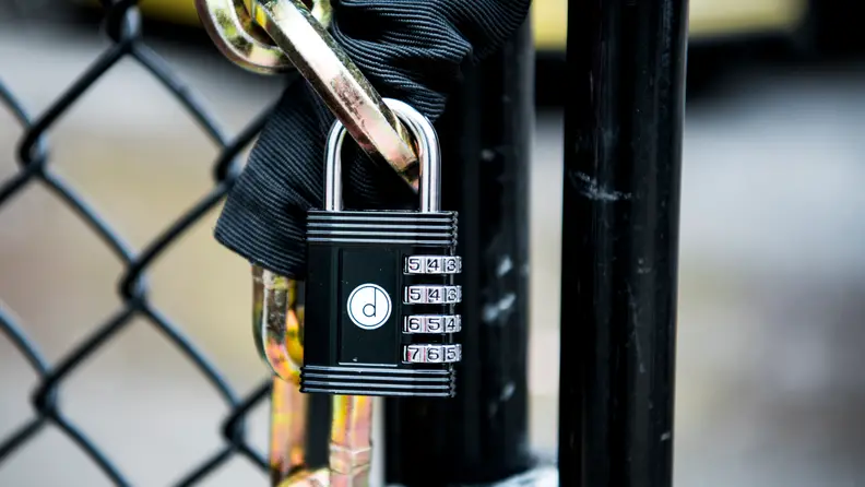 Desired Tools 4 Combination Padlock affixed to a chain around a black chainlink fence