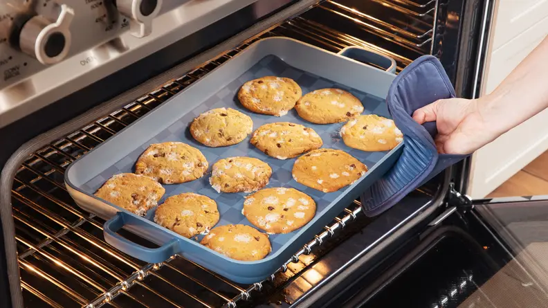 A hand pulls an Our Place tray of cookies out of an oven.