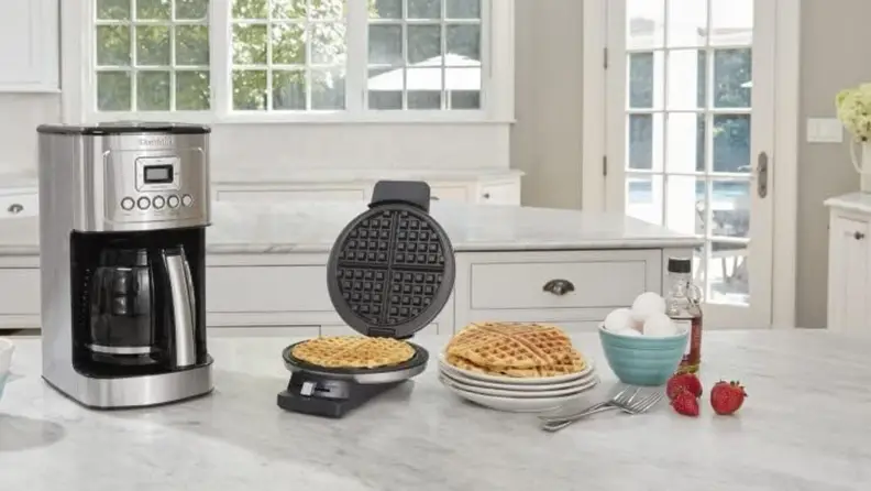 Cuisinart waffle maker on marble kitchen counter, surrounded by prepared waffles and coffee maker
