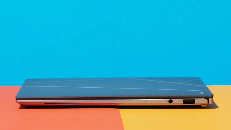 A side-view of a closed laptop aganist a colorful background