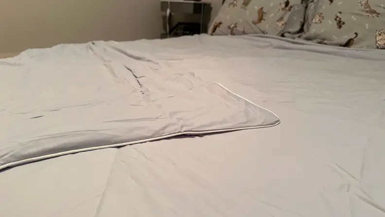 Close-up view of a gray Cozy Bliss comforter spread out on a bed with one corner folded over, in front of a beige wall.