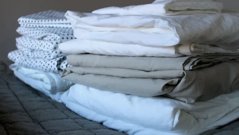 Five sets of the best percale sheets folded and stacked on a mattress.