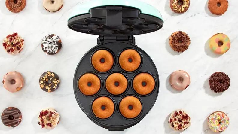 Mini donuts in the Dash Express Mini Donut Maker surrounded by an assortment of iced mini donuts.