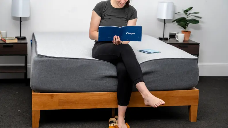 a woman sits on the edge of the casper select reading a brochure on the mattress