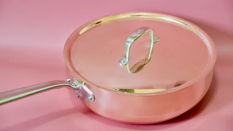 A copper pot with a lid on a pink background.