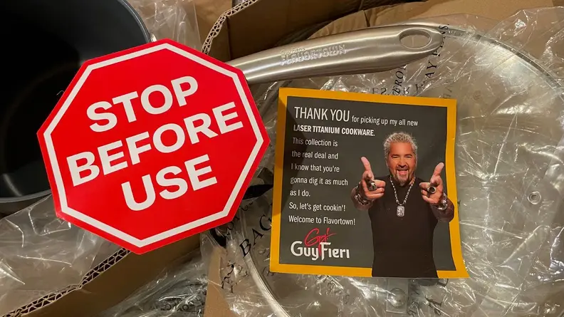 A paper stop sign and a thank you note from Guy Fieiri on top of a cookware set inside of plastic packaging.