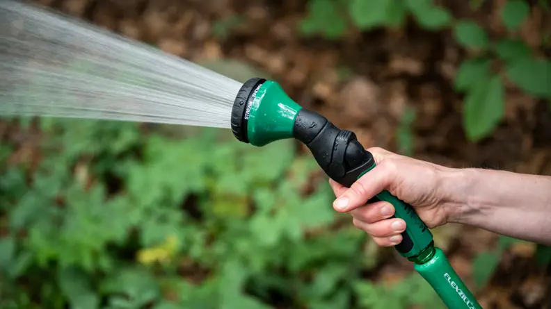 A person sprays water out of a green Dramm hose nozzle.