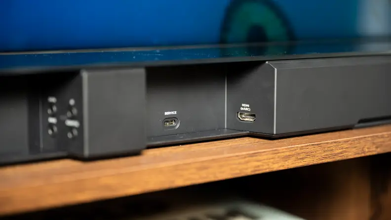 The back inputs section of a black soundbar reveals an multiple 3.5mm inputs including ports for bass, IR, data, and Adaptiq