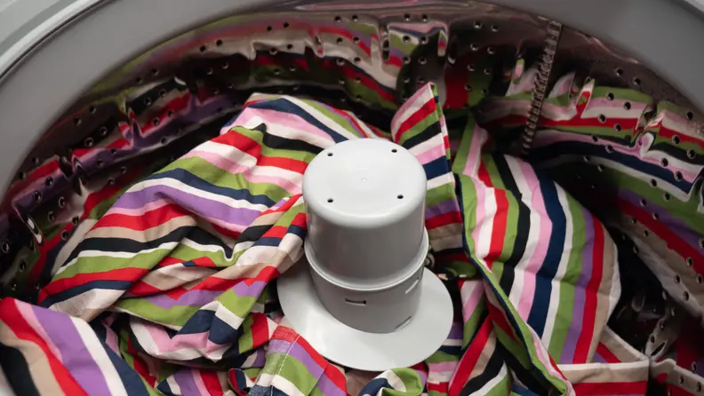A close-up of the Frigidaire FFTW4120SW washing machine's drum, with a rainbow comforter included for a sense of scale and a pop of color. The comforter takes up most of the drum, though the pole agitator can still be seen poking out.